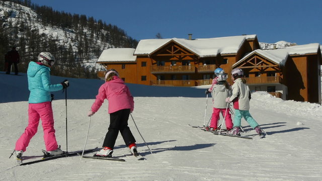 Young teenage girls learning Herringbone ski climbing technique lesson from instructor, up in the hill, with background mountain range on sunny day.

