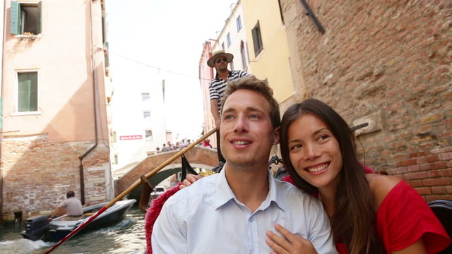 Tourists travel couple in Venice on Gondole boat ride enjoying romance in boat happy together on vacation holidays. Romantic young beautiful couple sailing in venetian canal in gondola. Asian woman.
