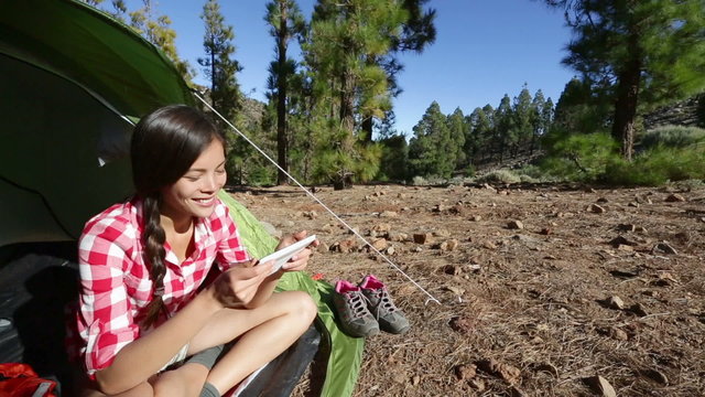 Tablet pc - camping girl taking selfie photo selfportrait at campsite in tent in forest. Beautiful young smiling happy mixed race Asian Caucasian woman model in outdoor activity