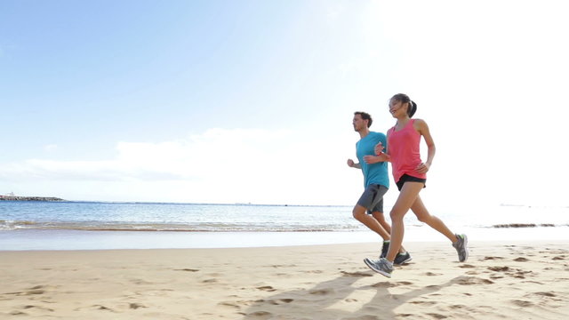 Runners running on beach. Jogging couple training on beach in full body length living healthy active lifestyle. Asian runner woman and fit male fitness athlete on run.