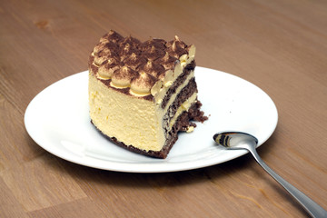 Breakfast. A piece of sponge cake on a white plate with teaspoon on the wooden table surface. Top view closeup