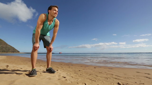 Running sports athlete runner man on beach stopping sweating and starting jogging. Fit exercising male fitness athlete model working out on beautiful beach training for marathon run.