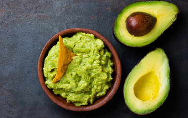 Traditional latinamerican mexican sauce guacamole in clay bowl and avocado on dark background. Top view
