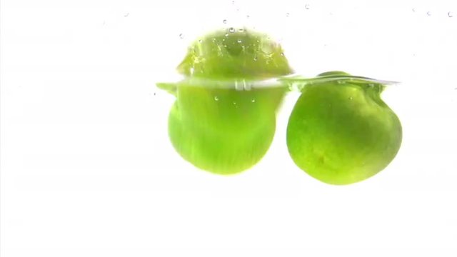 Fresh green apples falling into water then floating and bobbing around.