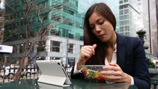 Business woman using tablet computer pc eating salad on lunch break in City Park living healthy lifestyle. Happy smiling mixed Asian young businesswoman, Bryant Park, Manhattan, New York City, USA