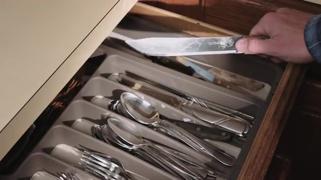 a person opens the utensils silverware drawer and grabs a long knife. Shimmers in light.