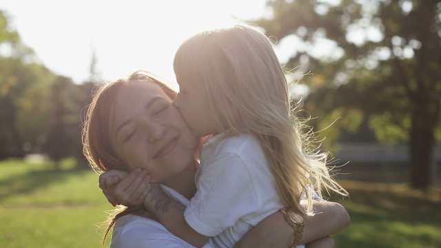 Mother with daughter hugging and kissing at nature at sunset