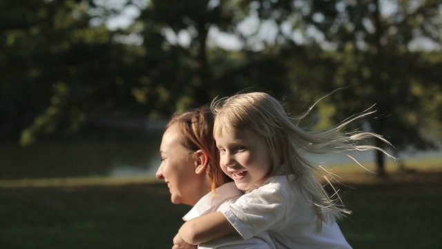 Daughter riding at mother in a city park at sunset.