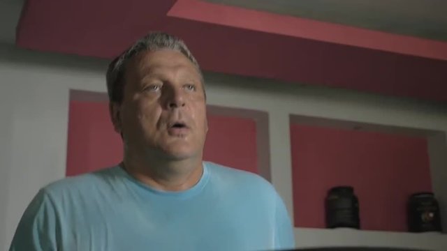 Slow motion of a senior man running on treadmill in fitness center. He is tired, sweat drops on the face. Sport nutrition in the background