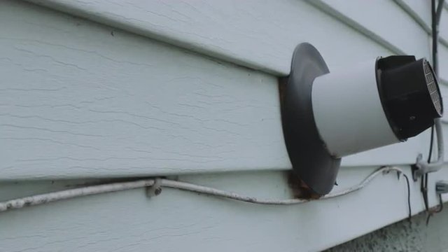 camera moves from the side of the house to reveal a closeup of a tankless water heater vent out of the side of the house