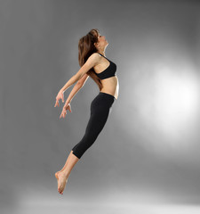 Fototapeta premium Young sporty woman jumping on grey background