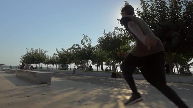 Slow motion steadicam shot of parkour man doing tricks in the city. He running and sliding on stone benches and making somersault in bright sunlight