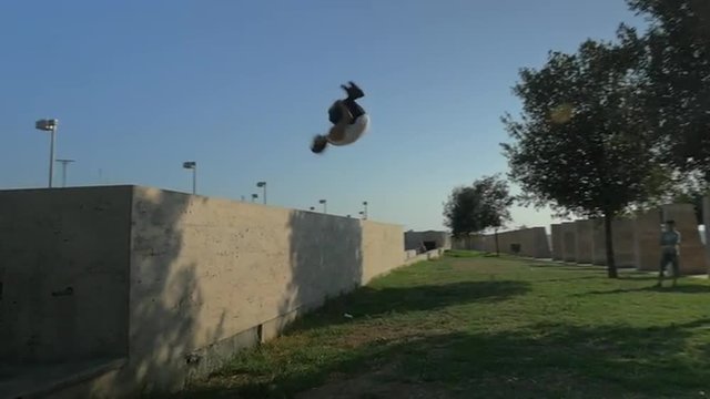 Slow motion steadicam shot of doing dangerous parkour trick. Young man jumping from the wall and doing somersault in the air. Thirst for adrenalin