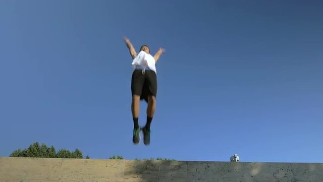 Slow motion steadicam shot of a young athlete performing somersault in a jump from the wall on blue sky background. Extreme hobby