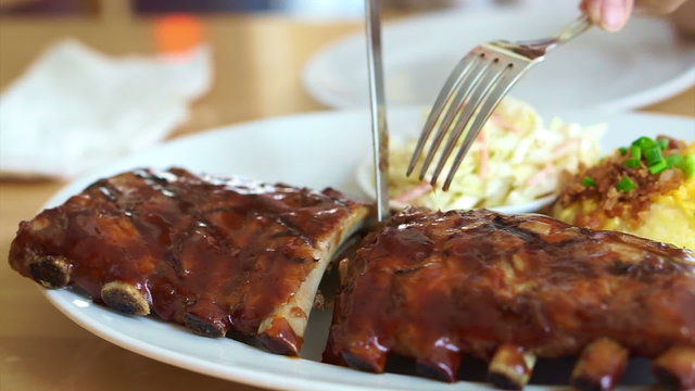 Video hands with knife and fork cutting baby pork ribs spare with barbecue sauce