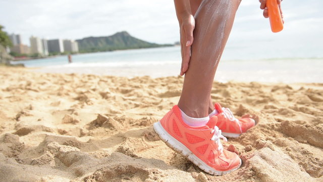 Sun Screen Lotion On Beach - Runner Athlete Woman Applying Sunscreen Suntan Lotion On Legs Using Bottle. Sporty Fitness Girl Putting Sun Protection On Legs Before Running. Waikiki, Oahu, Hawaii.  