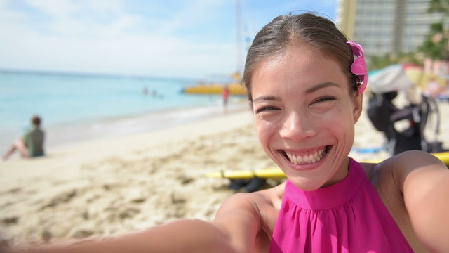Selfie beach travel woman self portrait video on Waikiki beach smiling happy in slow motion blowing a kiss and give wink to camera. Multiracial Caucasian Asian girl in Honolulu, Oahu, Hawaii, USA.