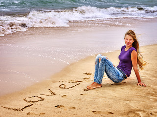 Fototapeta na wymiar Summer girl sea. Teenager draw love on sand near waves.