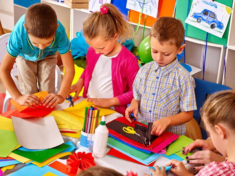 Group kids holding colored paper on table in preschooler.