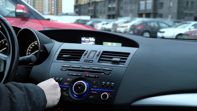 Мужчина настраивает радио автомагнитолы и регулирует громкость в автомобиле