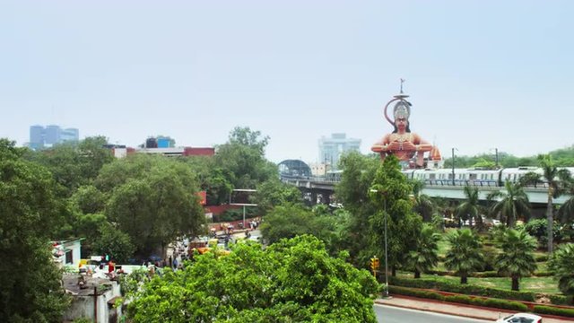 Locked-on shot of metro train moving in front of giant statue of Lord Hanuman, Karol Bagh, New Delhi, India 