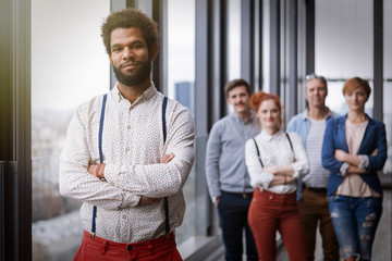 Corporate portrait of young black hipster businessman with his colleagues in background. Post processed with vintage film and sun filter.