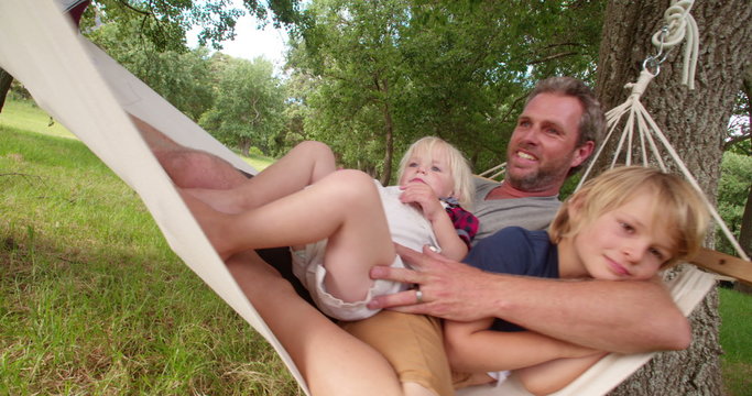 Cheerful dad cuddling his son on a white hammock