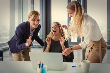 Three business women in modern office celebrating good project results. Post processed with vintage film filter.