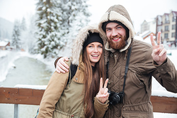 Couple with photo camera showing peace gesture on winter resort
