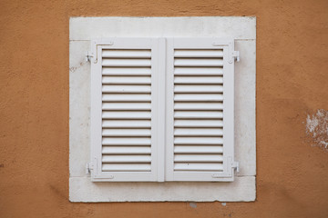 White window with shutters in yellow wall