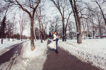 Fototapeta na wymiar Elegant stylish groom lift on his hands bride in snowy park
