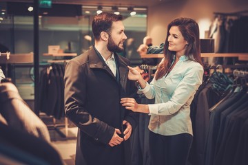Confident handsome man with beard choosing a coat in a suit shop.