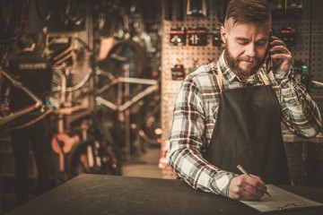 Stylish bicycle mechanic takes order by phone in his workshop.