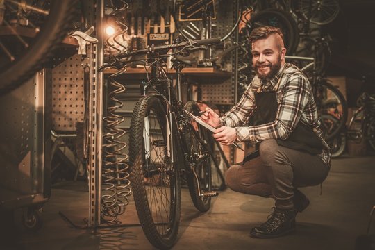 Stylish bicycle mechanic making notes in clipboard in his workshop.