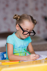 Joyful girl in glasses with a pen in hand is sitting at the table and learns lessons

