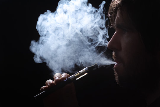 Young man smoking electronic cigarette on black background