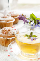Cup of green tea with lemon balm and tasty muffins with sugar hearts