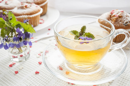 Cup of green tea with lemon balm and tasty muffins with sugar hearts