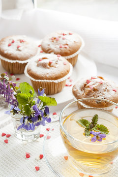 Cup of green tea with lemon balm and tasty muffins with sugar hearts