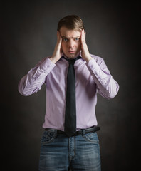 Portrait of pensive young man in pink shirt and dark tie with surprised face, against dark background.
