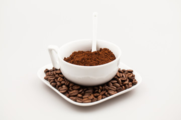 White coffee cup, coffee plate and teaspoon with coffee beans and coffee powder