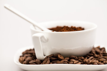 White coffee cup, coffee plate and teaspoon with coffee beans and coffee powder