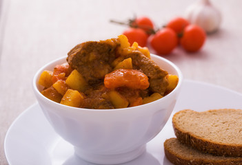 Homemade goulash with slices of bread in white bowl
