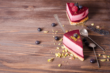 Piece of delicious raspberry cake with fresh raspberries, blueberry, currants and pistachios on shovel, wooden background. Free space for your text.