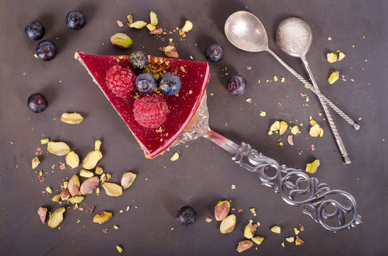 Piece of delicious raspberry cake with fresh raspberries, blueberry, currants and pistachios on shovel, black background. Free space for your text.
