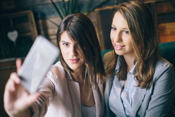Two beautiful young woman sitting at cafe and making selfie