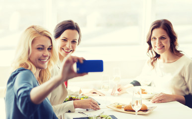 Fototapeta premium women with smartphone taking selfie at restaurant