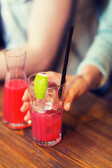 close up of hand with cocktail or juice and straw 
