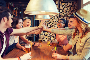 happy friends with drinks making high five at bar
