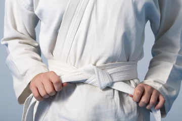 Fotobehang Vechtsport Handen die witte riem aanhalen op een tiener gekleed in kimono voor vechtsporten